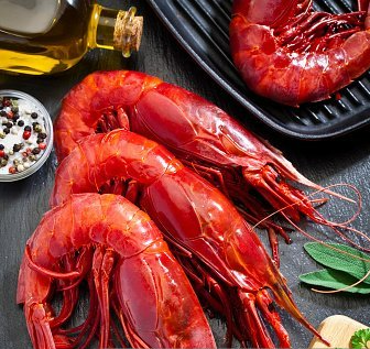 A bunch of red shrimp are sitting on a black plate on a table.