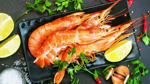 A black plate topped with shrimp , limes , garlic and parsley.