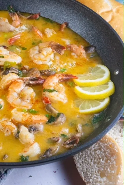 A pan filled with shrimp , mushrooms , and lemon slices.
