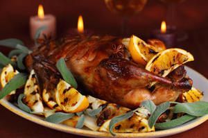 A roasted turkey with oranges and sage on a plate with candles in the background.