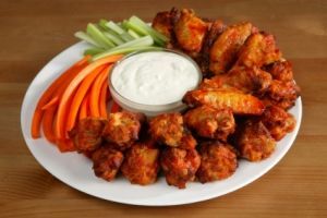 A white plate topped with chicken wings carrots celery and ranch dressing.