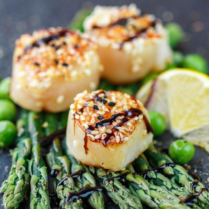 A close up of a plate of food with scallops and asparagus