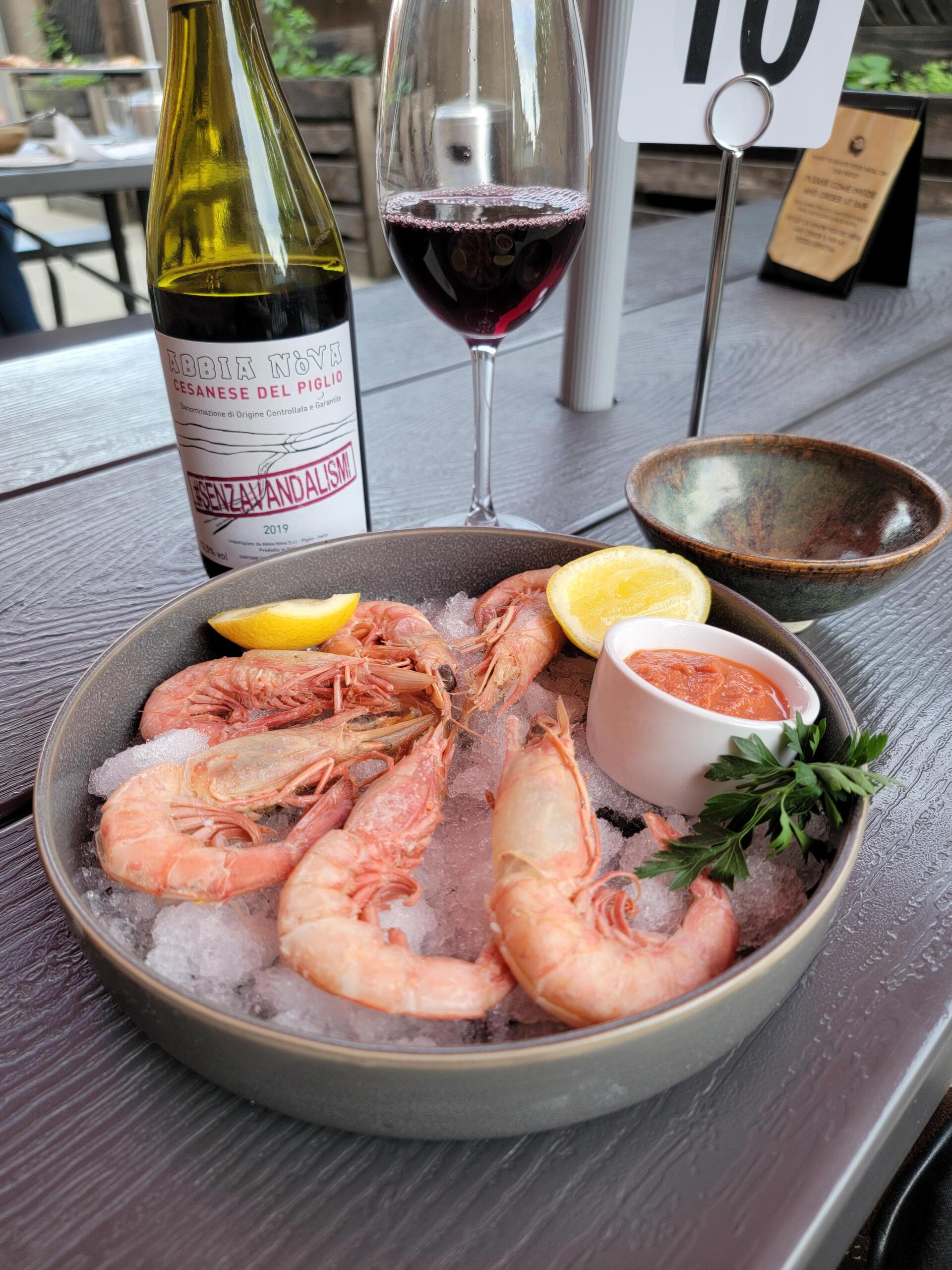 A bowl of shrimp on ice next to a bottle of wine and a glass of wine.