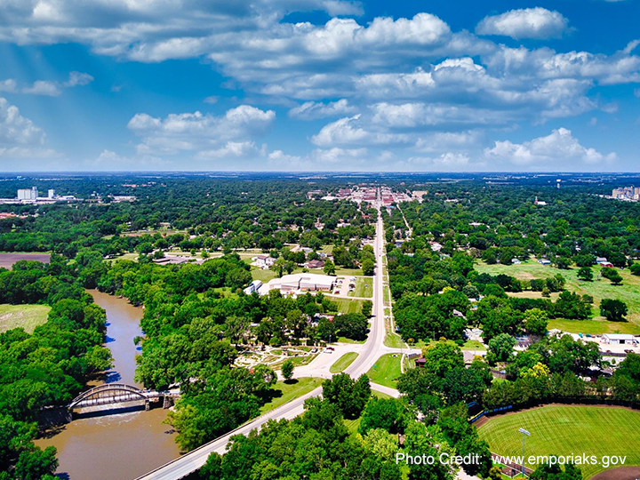 An aerial view of a river surrounded by trees and a bridge leading to a city.