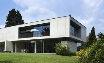 A modern house with a lot of windows is sitting on top of a lush green hillside.