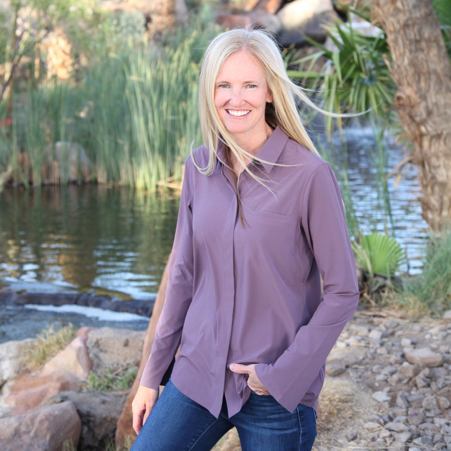 A woman in a purple shirt is standing in front of a river