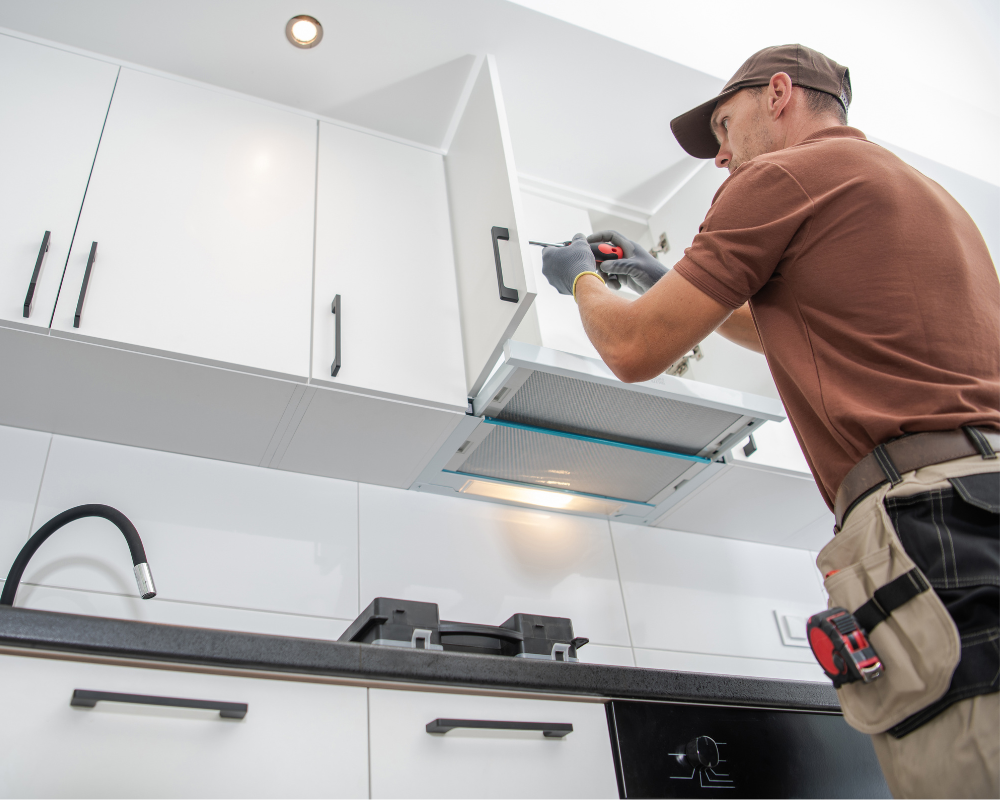 A man is working on a kitchen hood with a drill.