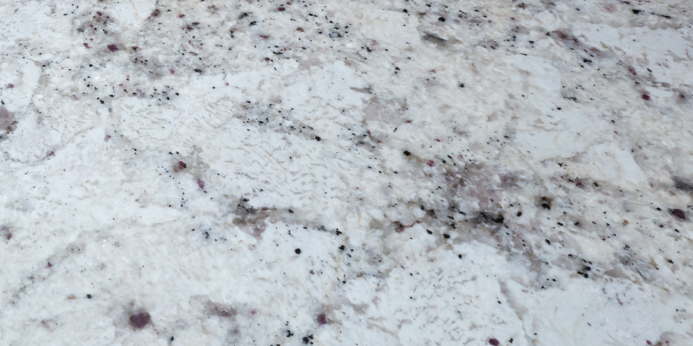 A close up of a white granite counter top with black spots.