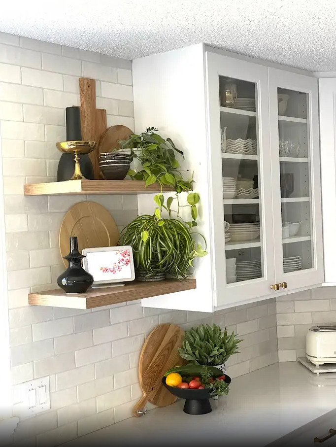A kitchen with white cabinets , glass doors , wooden shelves and a bowl of fruit on the counter.