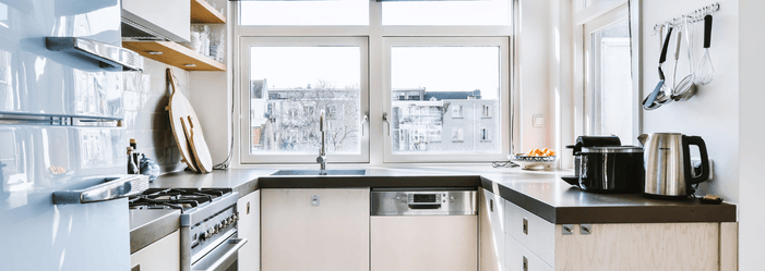 A kitchen with white cabinets , a stove , a sink , and a window.