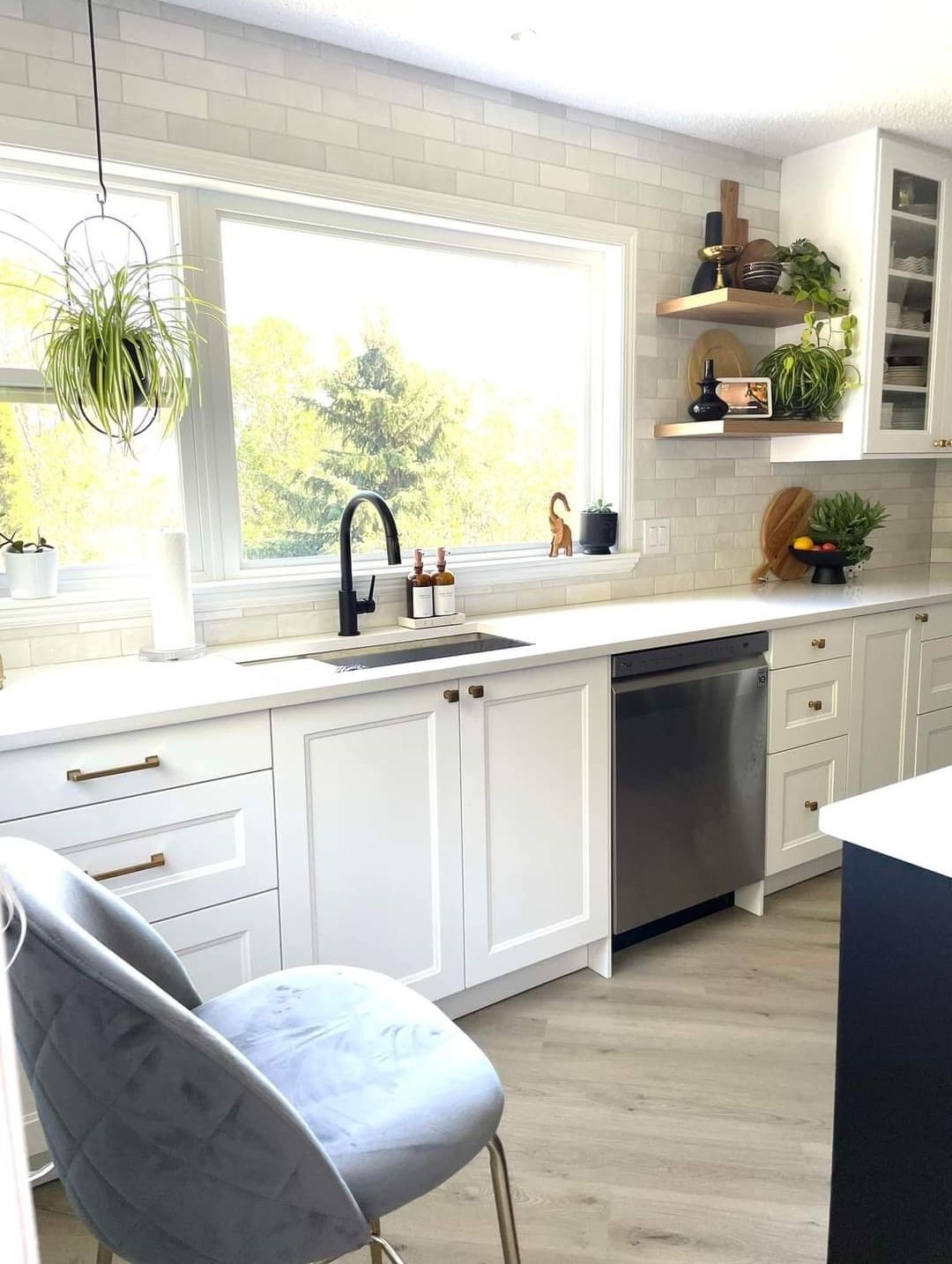 A kitchen with white cabinets , stainless steel appliances , a sink , and a chair.