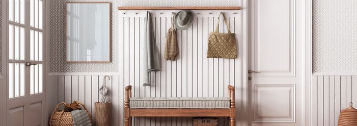 A hallway with a bench , a mirror , and a coat rack.