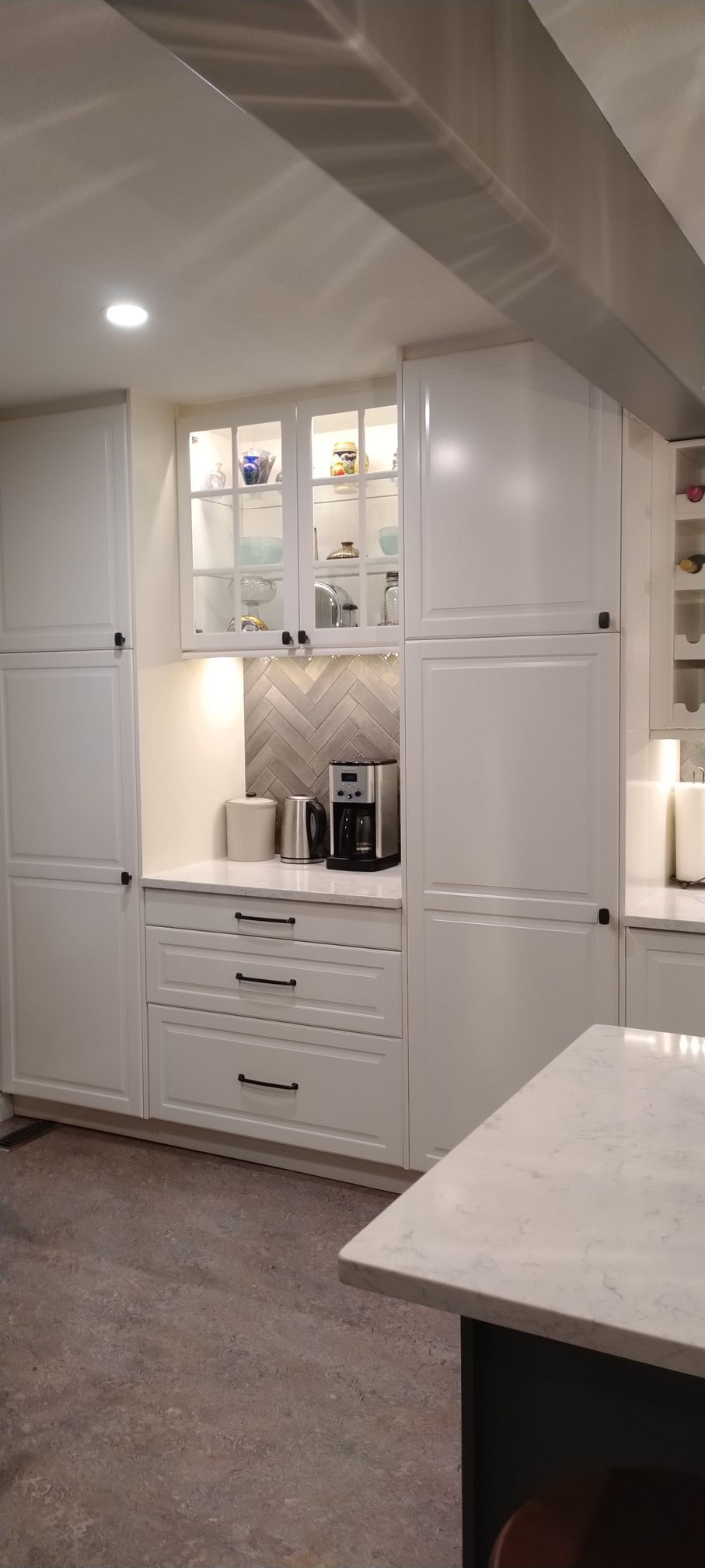 A kitchen with white cabinets , white counter tops , and a coffee maker.