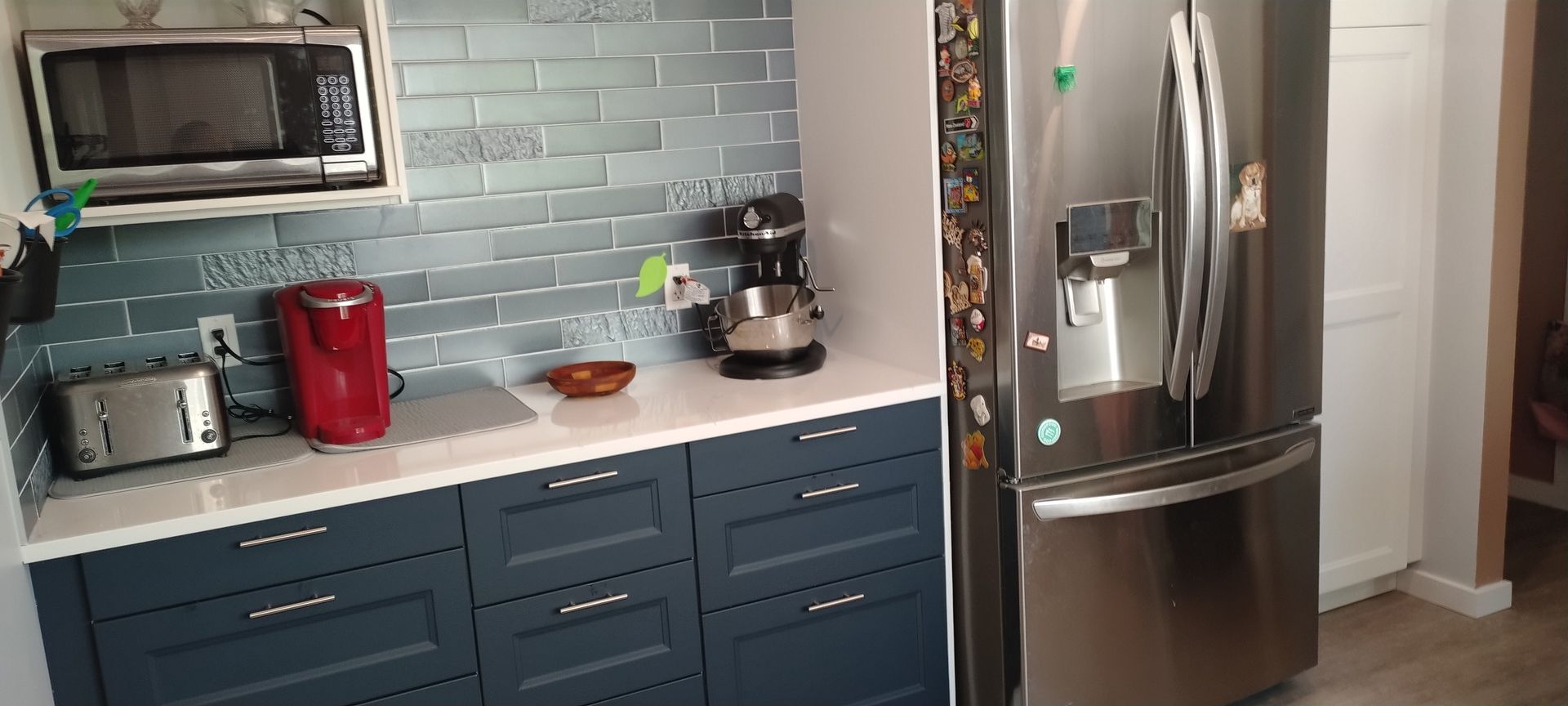 A kitchen with blue cabinets , a stainless steel refrigerator and a microwave.