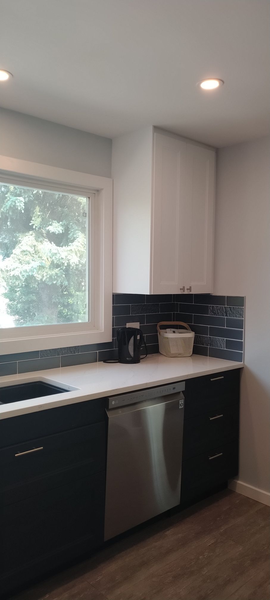A kitchen with black cabinets , stainless steel appliances , a sink , and a window.