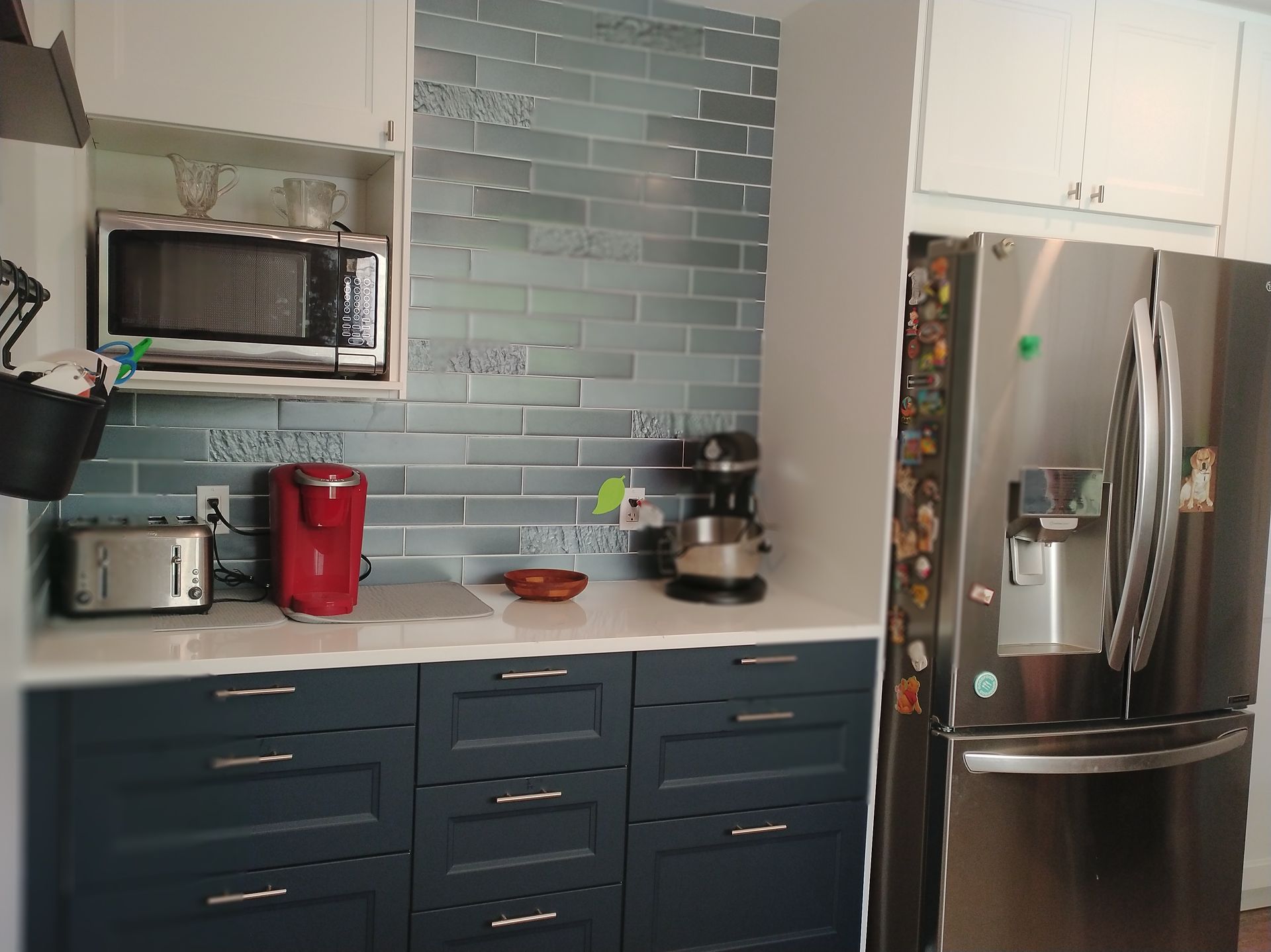 A kitchen with blue cabinets , stainless steel appliances , a microwave and a refrigerator.