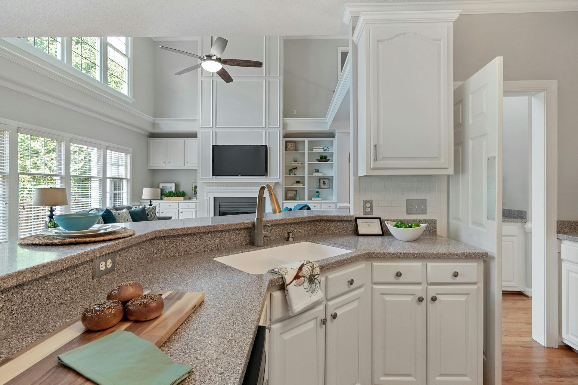 A kitchen with granite counter tops , white cabinets , a sink and a ceiling fan.