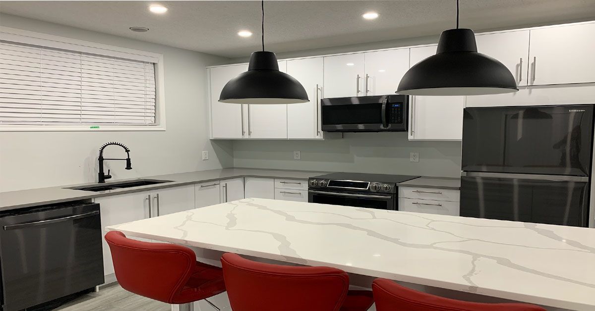 A kitchen with white cabinets , black appliances , a large island , and red chairs.