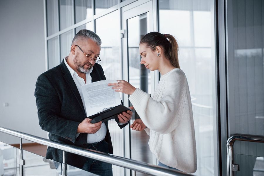 Two colleagues reviewing a document together in a bright office hallway