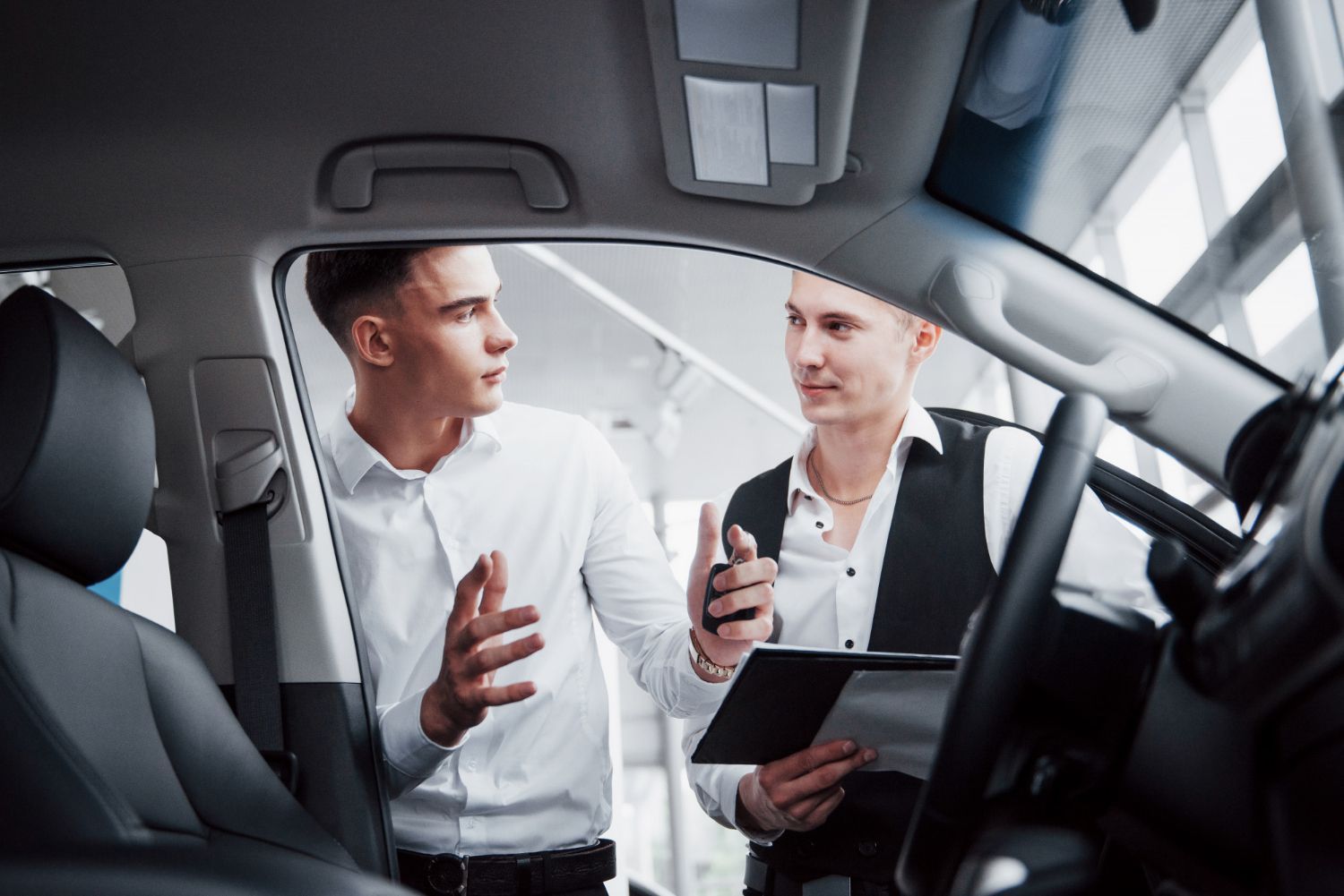 Two people discussing a tablet and phone inside a car dealership showroom
