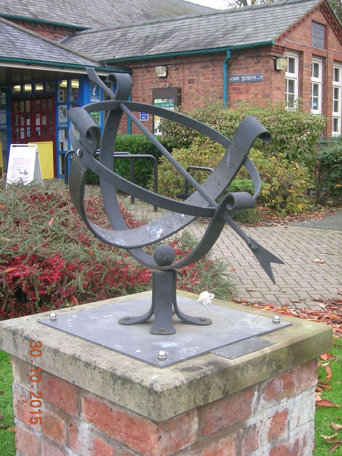 A sundial is sitting on a brick post in front of a brick building.