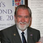 Chris Tandy in a suit and tie is standing in front of a sign.