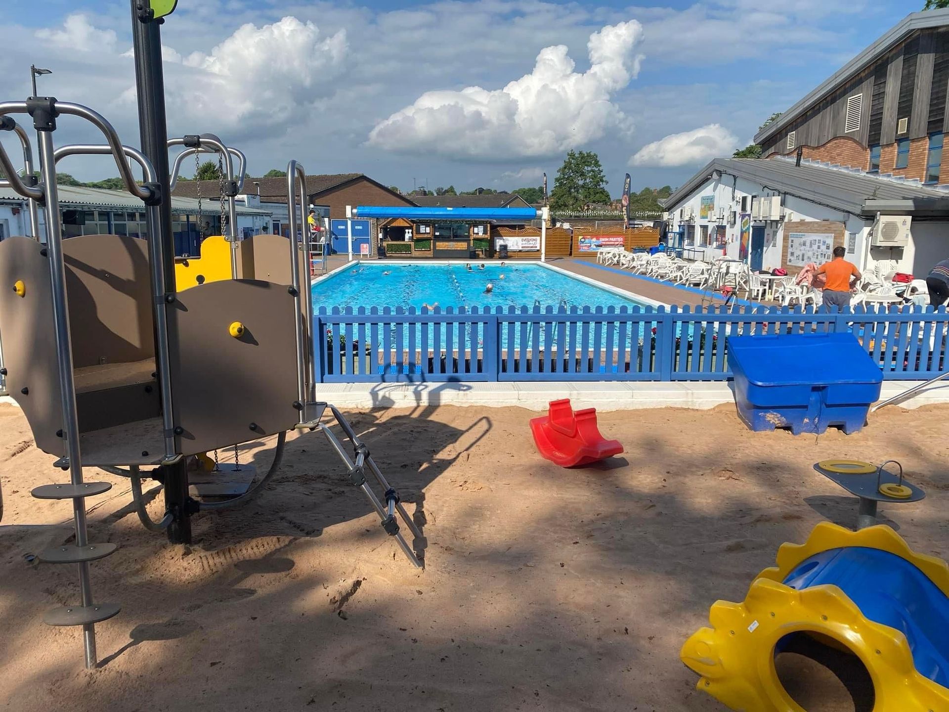 A playground with a fence and a pool in the background.
