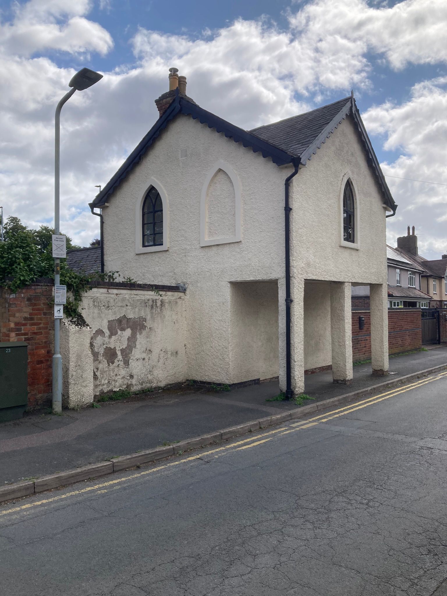 A small white building with a black roof is sitting on the side of a road of the Priest House 2024.