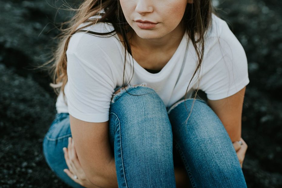 Person crouching outdoors in a white T-shirt and blue jeans on dark rocks