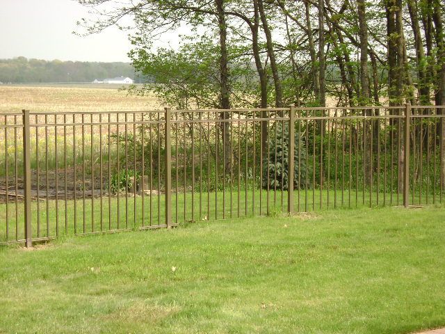 A metal fence surrounds a lush green field with trees in the background in Columbus