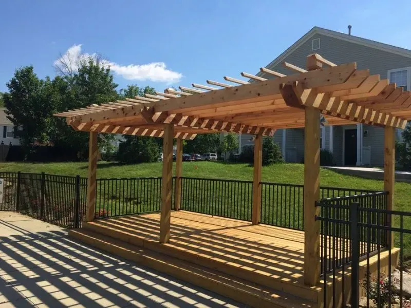 A wooden pergola is sitting on top of a wooden deck surrounded by a black aluminum fence in front of a house in Columbus