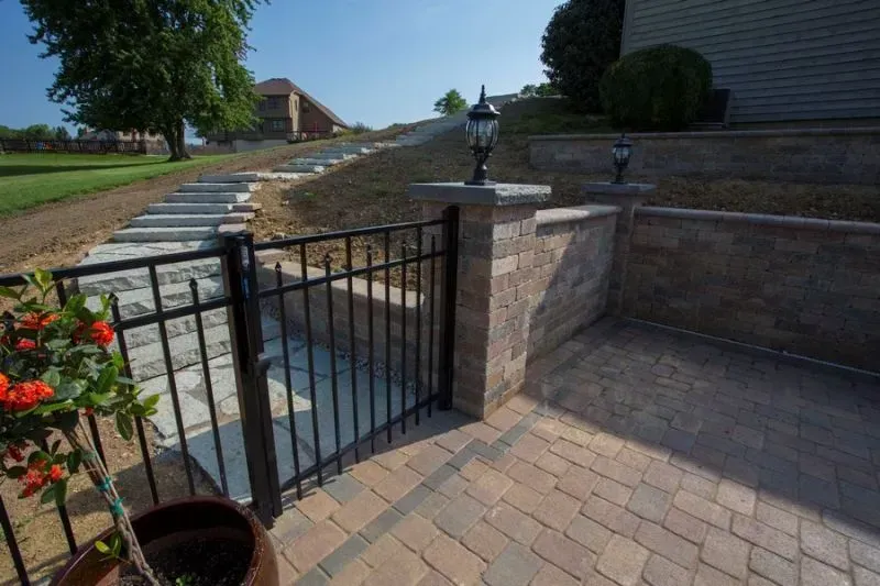 A brick walkway with an aluminum fence gate and stairs leading to a house in New Albany.