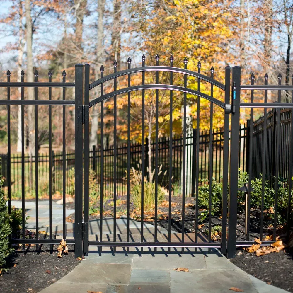 A black wrought aluminum gate is surrounded by a fence and trees in Columbus