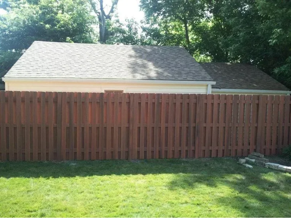 A wooden privacy fence standing in front of a white garage with a gray shingled roof and surrounding green trees in Columbus