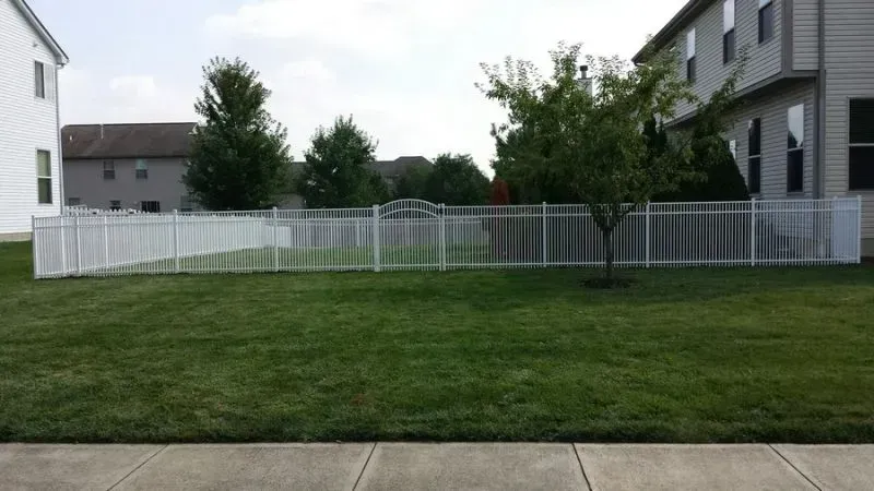 A white aluminium fence surrounds a lush green yard in front of a house in New Albany