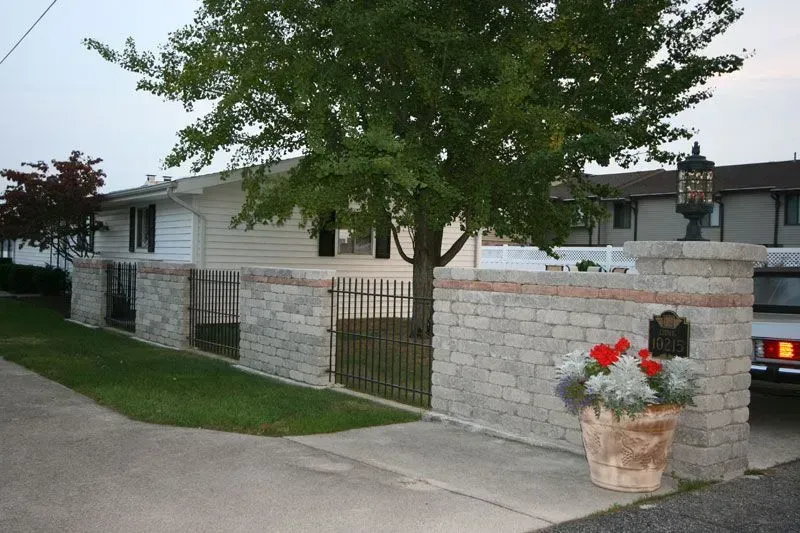 A car is parked in front of a house with a brick wall and aluminum fence in Columbus