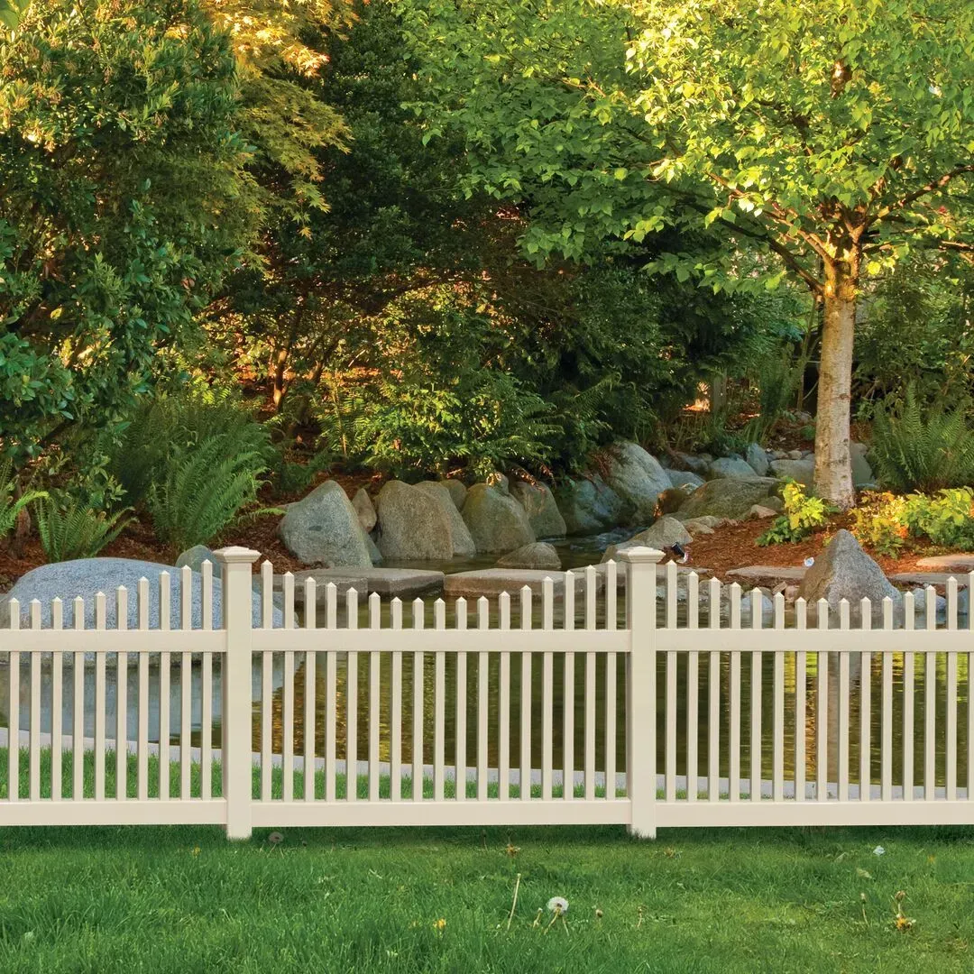 A white picket vinyl fence surrounds a lush green garden with trees and rocks in Columbus