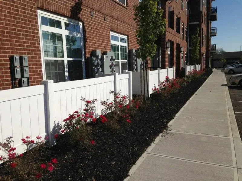 A white vinyl fence along a sidewalk in front of a brick building in Columbus