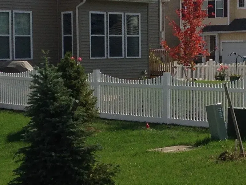 A white vinyl picket fence surrounds a lush green yard in front of a house in Columbus