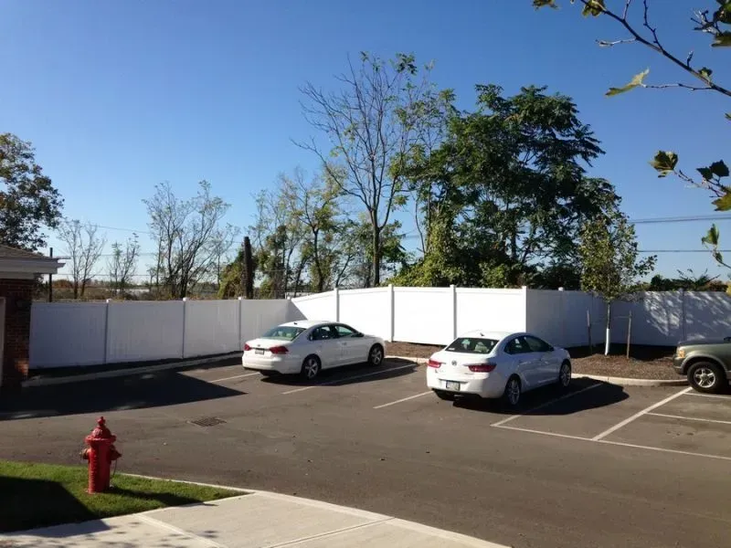 Two white cars are parked in a parking lot next to white vinyl fence in Columbus