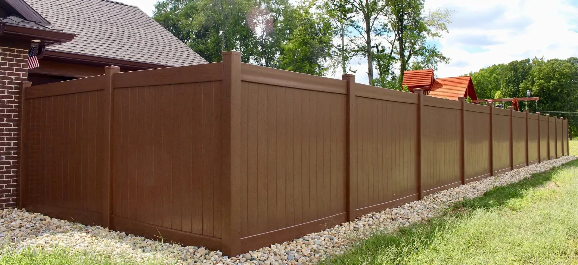 A brown wooden vinyl fence surrounds a grassy area in front of a house in Columbus