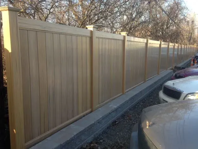 A wooden fence surrounds a parking lot with cars parked behind it in Hillard