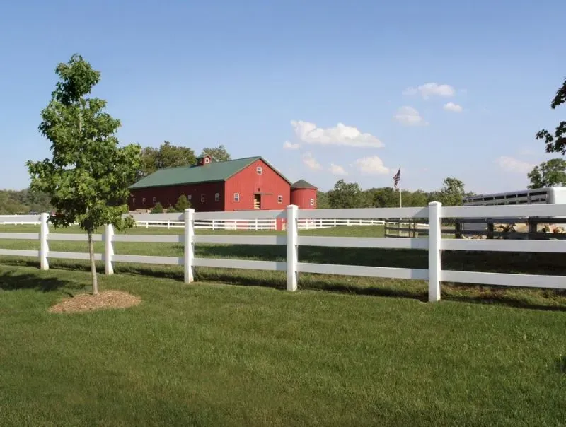 A white vinyl fence with a red barn in the background in New Albany.