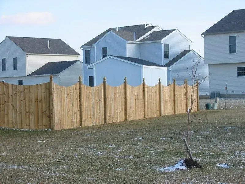 A wooden fence surrounds a grassy field with houses in the background in Columbus