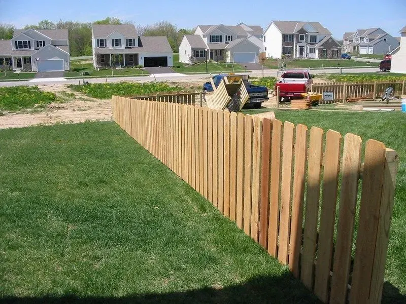 A wooden fence surrounds a lush green yard with houses in the background in Columbus