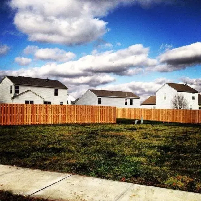 A wooden fence surrounds a grassy field with houses in the background in Columbus