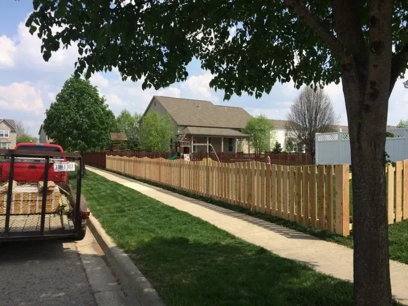 A red truck is parked on the side of the road next to a wooden fence in Columbus