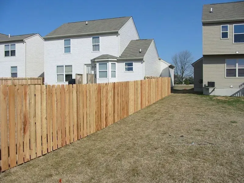 A wooden fence surrounds a yard with houses in the background in Columbus