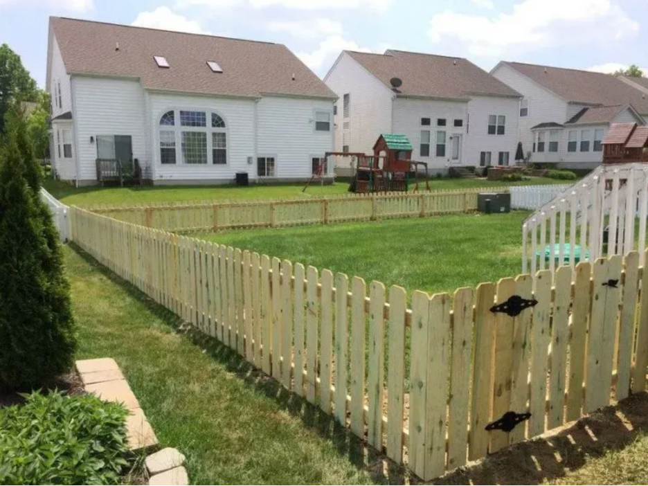 A new wooden picket fence encloses a green backyard lawn in front of several suburban houses on a sunny day in Columbus