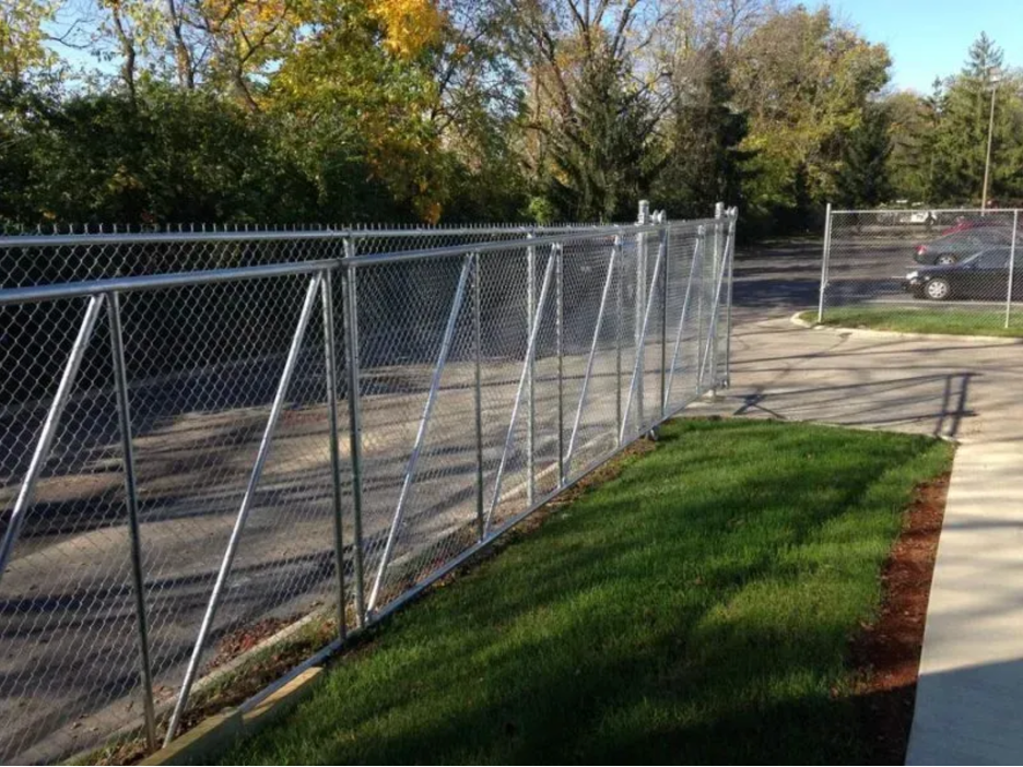 A tall chain-link fence bordering a grassy lawn and a paved parking lot under a clear blue sky in Columbus